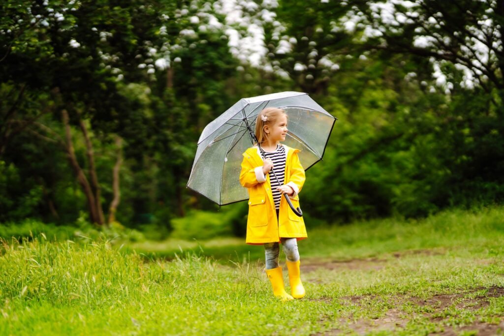 Little girl with transparent umbrella playing in rain on sunny. Beautiful girl in a yellow cloak