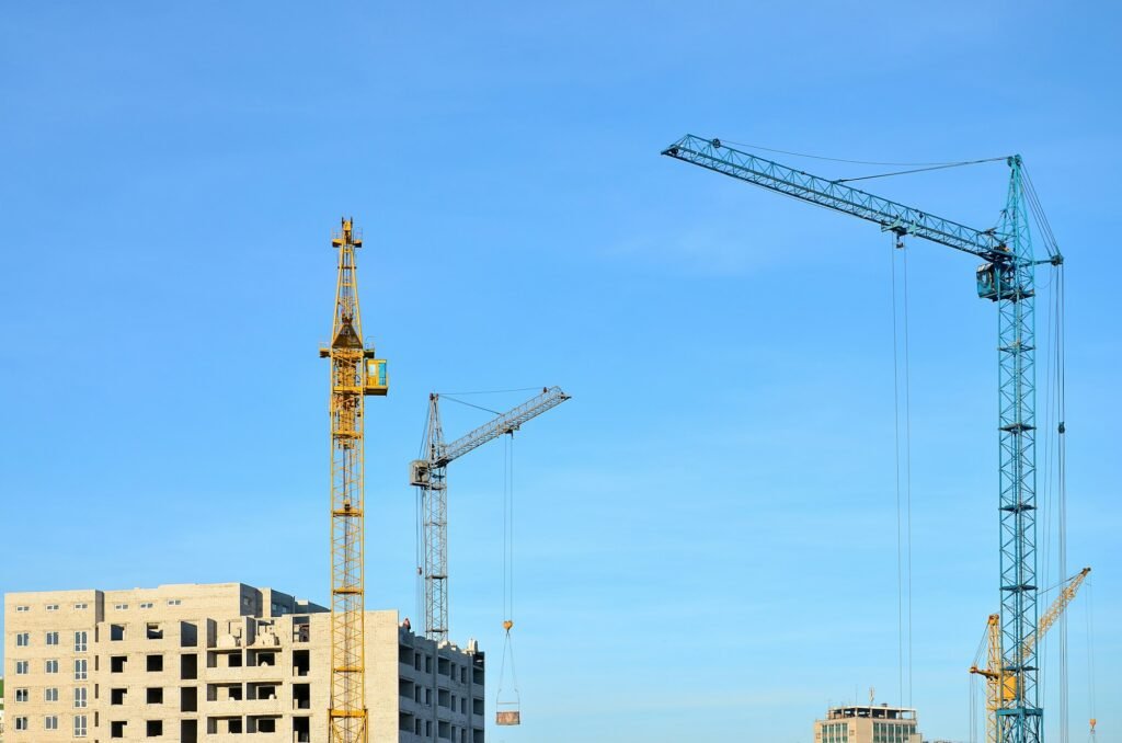 Working tall cranes inside place for with tall buildings under construction against a clear blue sky